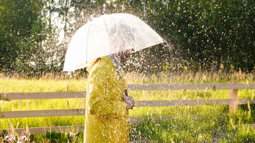A man in a yellow raincoat in the rain. It's raining and the sun is shining