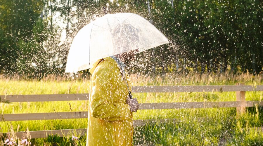 A man in a yellow raincoat in the rain. It's raining and the sun is shining